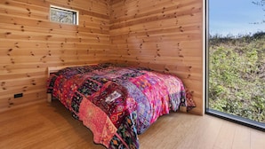 A room with wooden walls, a bed with a colorful quilt, a window, and a view of greenery outside. - 4 Star Holiday Home in Hasle (Hasle)