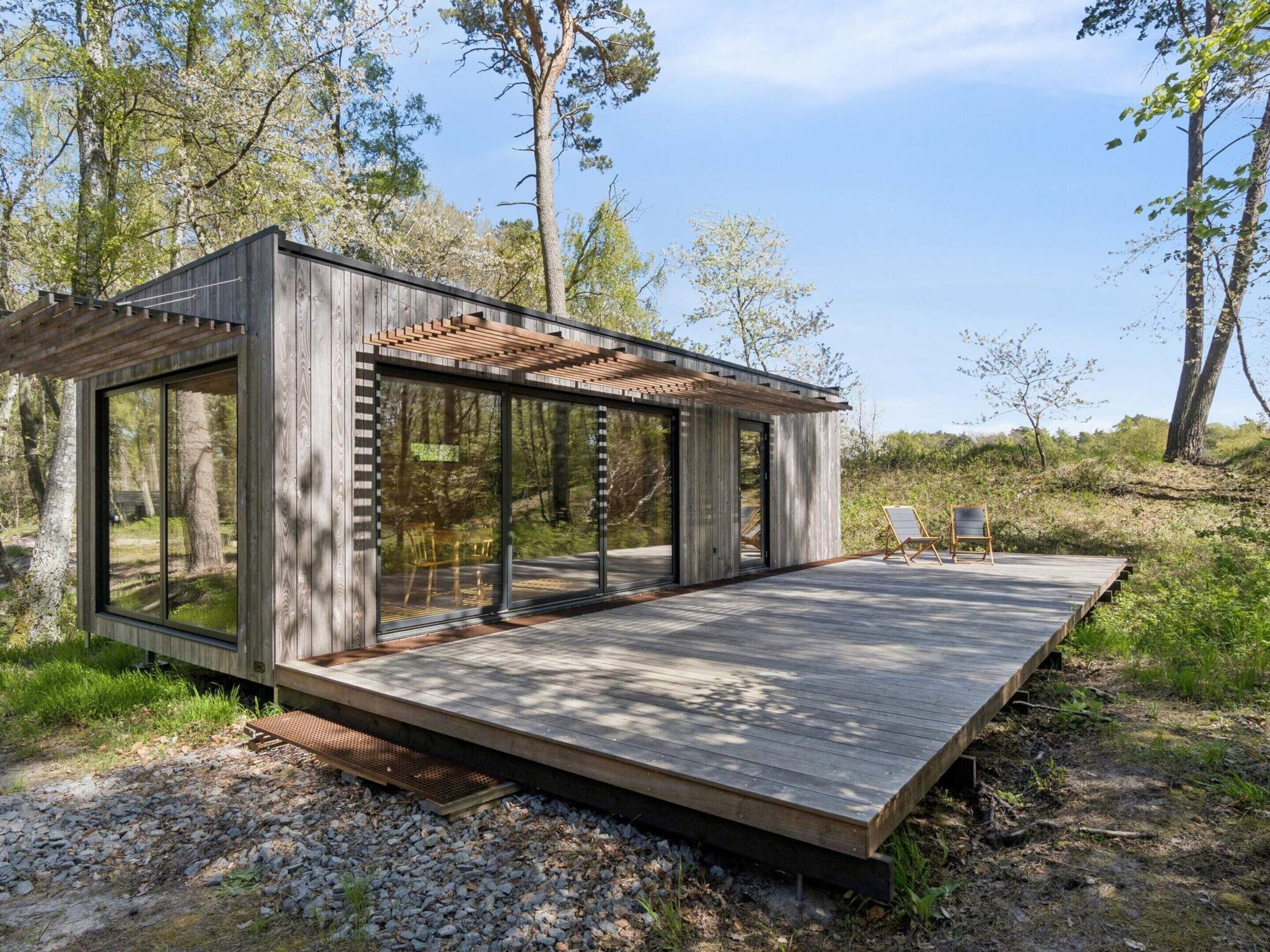 Una cabaña de madera moderna con amplios ventanales, una terraza y una pérgola.
