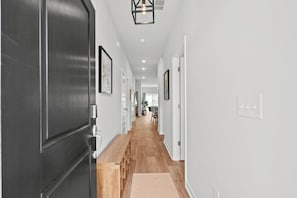 Un couloir avec un banc en bois, des œuvres d’art encadrées accrochées aux murs et une porte sur la gauche.