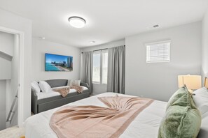 Quarto com cama, sofá, janela com persianas, quadro na parede e abajur.