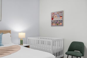 A white crib, a green chair, a bedside lamp, and a wall art piece.
