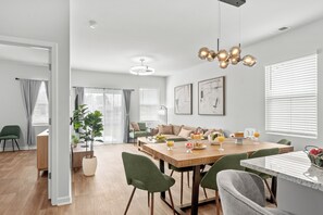 A modern dining area with a wooden table, green chairs, and a chandelier.