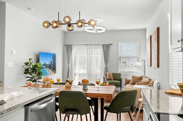 Une cuisine moderne avec un coin repas, une grande fenêtre avec des rideaux et un lustre.