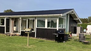 A modern house with a covered patio, a barbecue grill, and a white van parked outside.