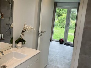 A bathroom with a white sink, a shower, and a door leading to a balcony with a view of greenery. - 4 Star Holiday Home in Skibby (Skibby)