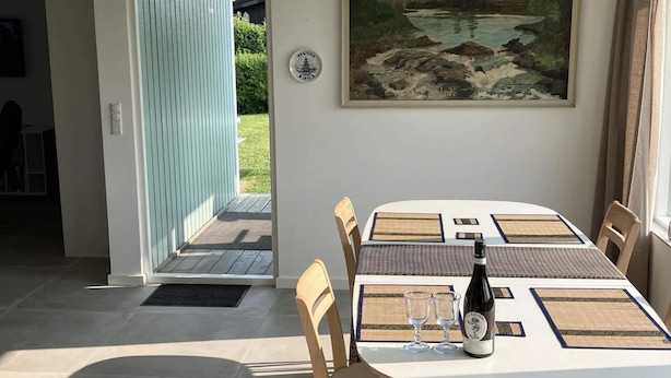 A dining area with a table set for two, a bottle of wine, and a painting on the wall.