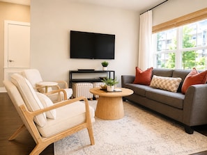 Un salon comprenant un canapé, un fauteuil, une table basse et un téléviseur à écran plat fixé au mur.