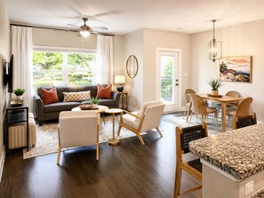 A living room with a sofa, chairs, a coffee table, a dining area with a table and chairs, a ceiling fan, and a door leading outside.