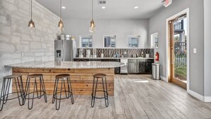 Una cocina moderna con una isla grande, taburetes de bar, luces colgantes y vistas al exterior.