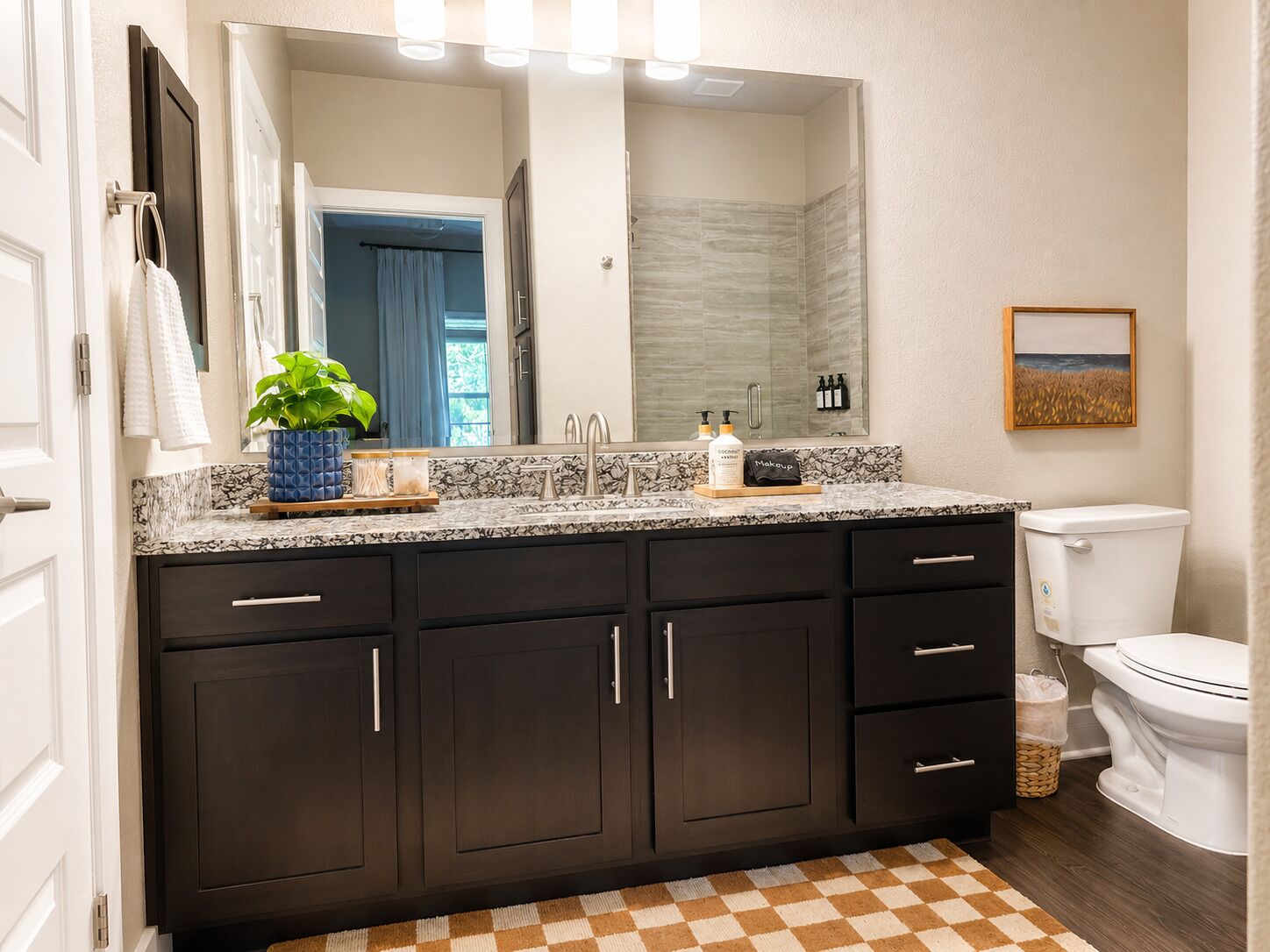 A bathroom with dark cabinets, a marble countertop, a sink, a toilet, and a checkered floor.