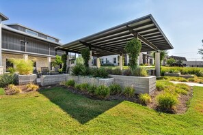 Een overdekt buitengebied met een modern ontwerp, met een pergola, plantenbakken met diverse planten en een verzorgd gazon.