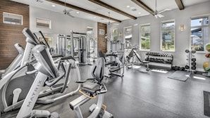 Un gimnasio con diversos equipos de ejercicio, ventanas amplias y un ventilador de techo.