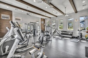 Een sportschool met diverse fitnessapparaten, grote ramen en een plafondventilator.