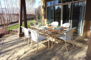 Un patio con un tavolo apparecchiato per quattro persone, circondato da sedie in vimini, una pianta in vaso e una porta in vetro che dà su una zona coperta.