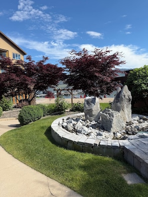 Un giardino curato con una fontana in pietra, un pergolato in legno e un edificio sullo sfondo.