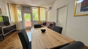 A room with a wooden dining table, chairs, a sofa, a television, and a door. - Large 3BR Apartment in the Center & Sand Beach 5BD (Split)