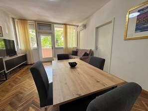 Ein Zimmer mit einem Holztisch, Stühlen, einer Couch, einem Fernseher und einer Tür.