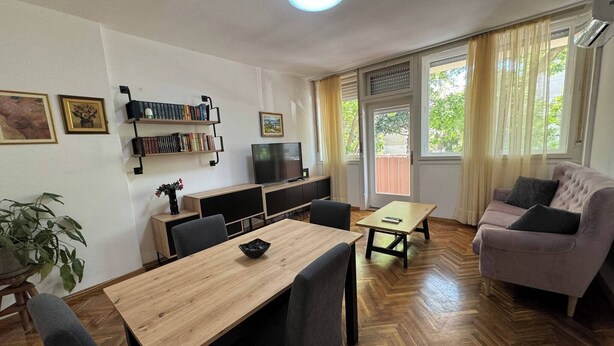 A living room with a wooden dining table, chairs, a sofa, a TV, and a bookshelf. - Large 3BR Apartment in the Center & Sand Beach 5BD (Split)