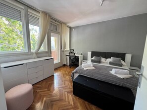 Ein Schlafzimmer mit Bett, Schreibtisch, Stuhl, einem Fenster mit Vorhängen und einer Heizung.
