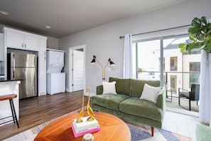 Un apartamento moderno con cocina, un sofá verde, una mesa de centro de madera y un balcón con vistas.