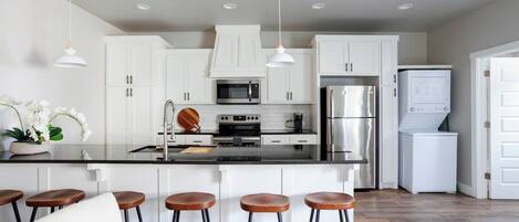 Una cocina moderna con armarios blancos, electrodomésticos de acero inoxidable y una isla central con taburetes.