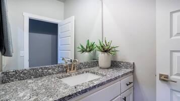 A bathroom with a granite countertop, a white sink, a gold faucet, and a potted plant.