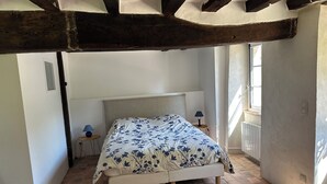 Un dormitorio con una cama, dos mesitas de noche, un ventanal y vigas de madera a la vista.