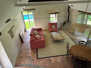 A spacious living area with a red sofa, a coffee table, and a dining table with chairs. There is a large window providing a view of the outdoors. - 2 country houses, sleeps 8, swimming pool (Saint-Denis-d'Anjou)
