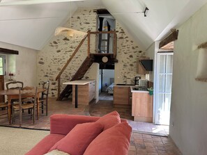 A loft-style room with a high ceiling, a stone wall, a wooden staircase, a kitchen area, and a dining table with chairs. - 2 country houses, sleeps 8, swimming pool (Saint-Denis-d'Anjou)