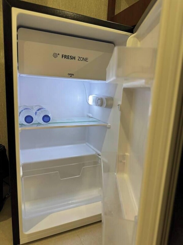 Een geopende koelkast met een 'FRESH ZONE' label, twee waterflessen en een wijnkoeler.