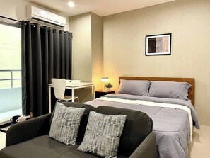 Ein Hotelzimmer mit Bett, Schreibtisch, Sessel, Sofa und einem Fenster mit Vorhängen.