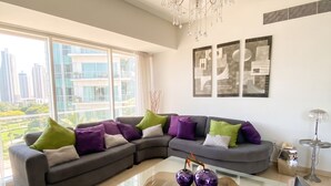 Een moderne woonkamer met een hoekbank, een glazen salontafel en een kroonluchter.