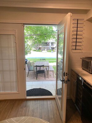 A kitchen with a microwave, a dining area with a table and chairs, and a view of a residential area through a glass door.