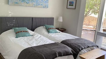 Une chambre avec deux lits, un ventilateur de plafond, un tableau et une fenêtre avec des stores.
