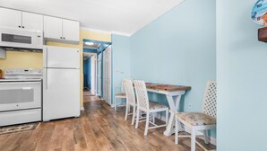 Una cocina con electrodomésticos blancos, un comedor con mesa y sillas, y un pasillo que conduce a otra habitación.