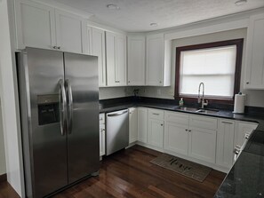 A kitchen with white cabinets, a stainless steel refrigerator, a dishwasher, a sink, and a window with blinds.