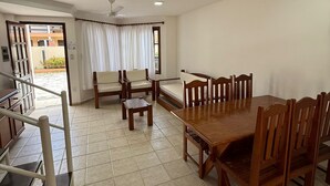 A dining area with a wooden table and chairs, a ceiling fan, and a view through a window with curtains. - Village dos bosques 43 (Porto Seguro)