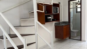 A modern staircase with white railings and dark steps, leading to a kitchen area with a sink and cabinets. - Village dos bosques 43 (Porto Seguro)