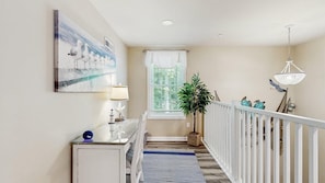 A hallway with a white railing, a potted plant, a painting, and a lamp. - The Foxes Den (Ocean Pines)