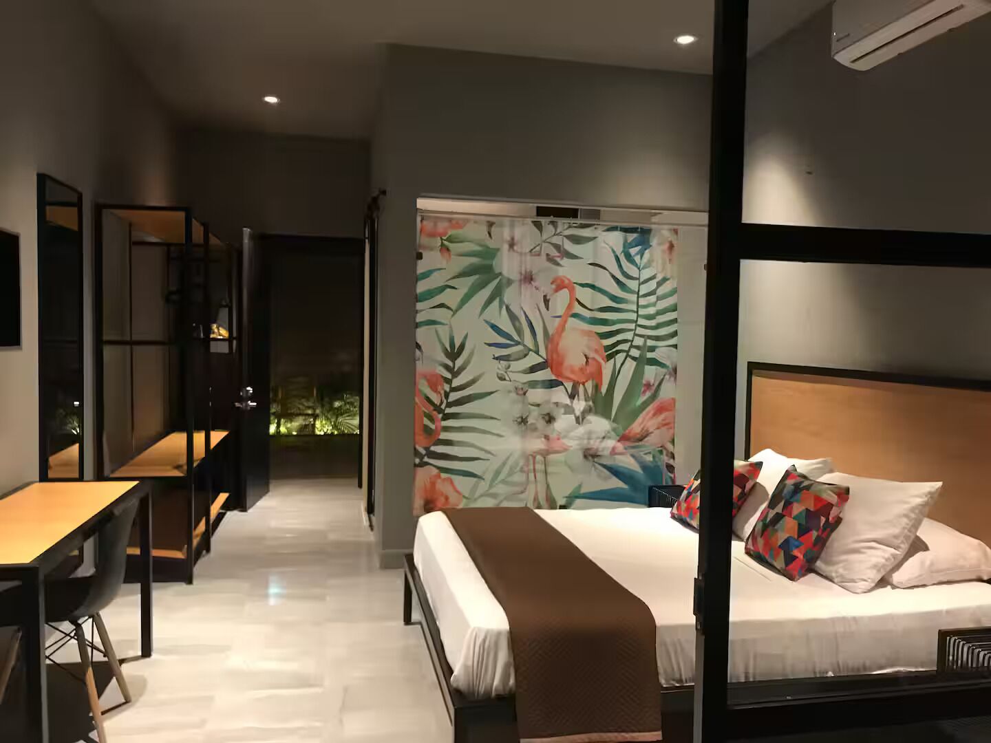 A modern hotel room with a bed, a desk, and a view of the outside.