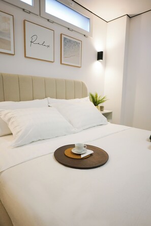 A neatly made bed with white bedding, a tray with a cup and saucer, and framed artwork on the wall.