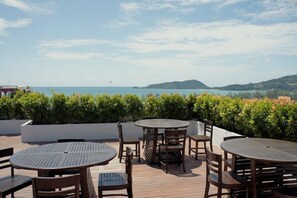 Una terraza con mesas y sillas de madera redondas, con vistas a un cuerpo de agua y colinas.