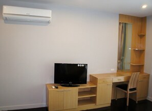 Una habitación con un escritorio de madera, televisión, una silla y estantería empotrada.