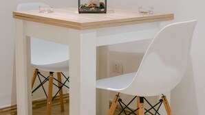 Un tavolo bianco con piano in vetro, una sedia bianca con gambe in legno e un quadro incorniciato sul tavolo.