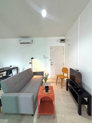 A living room with a sofa, a coffee table, a TV stand, and a door. - 1minBTS-Wifi500Mbs-Workplace>NETFLIX/Central (Khlong Toei)