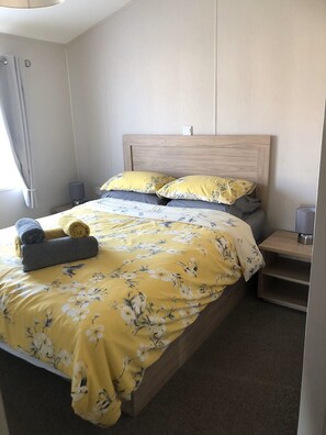 Cama bem arrumada com roupa de cama florida, duas almofadas e toalhas dobradas.