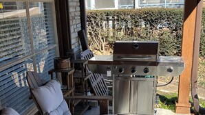 A patio with a grill, outdoor seating, and a view of a house.