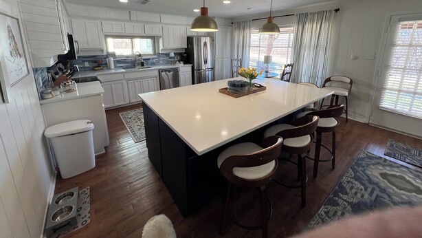 A modern kitchen with white cabinets, a central island, bar stools, and pendant lighting.