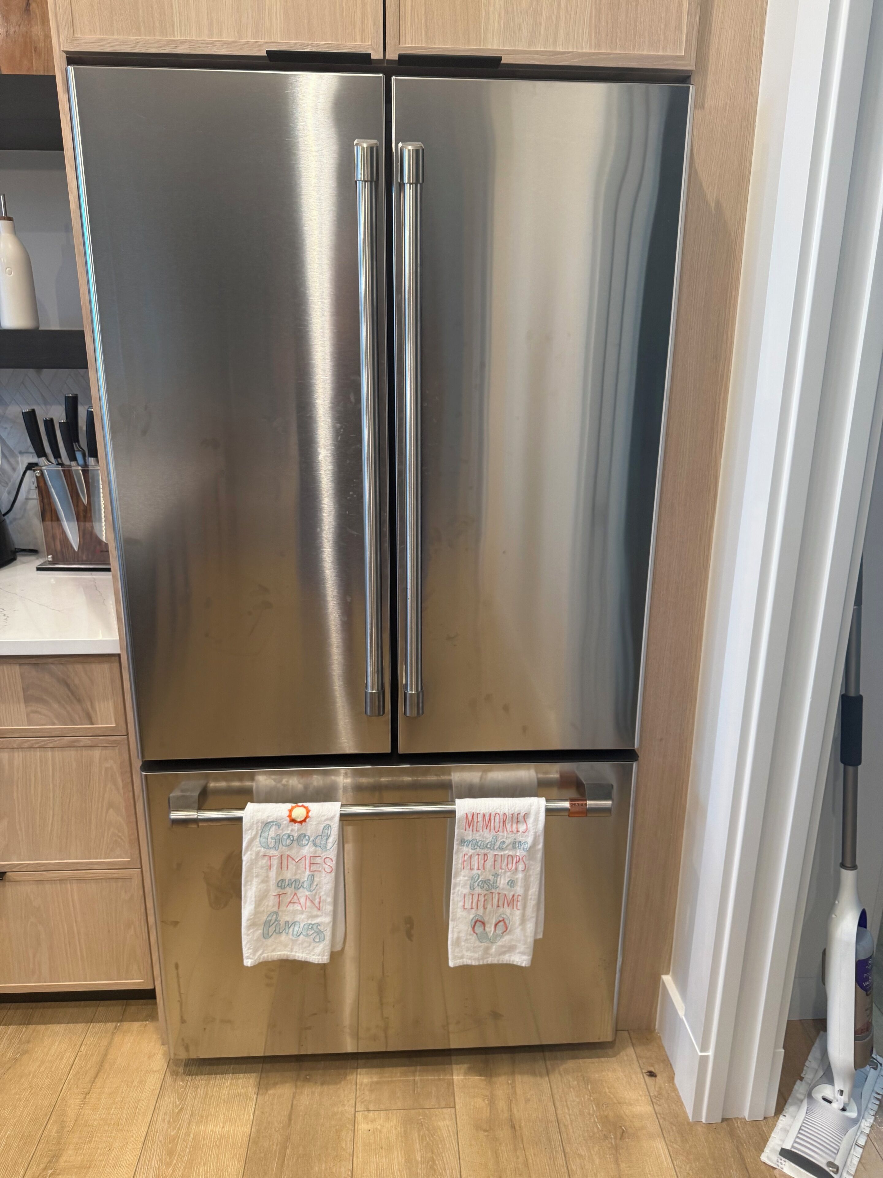 Een koelkast met dubbele deuren van roestvrij staal in een keuken met houten kastjes en een aanrecht.