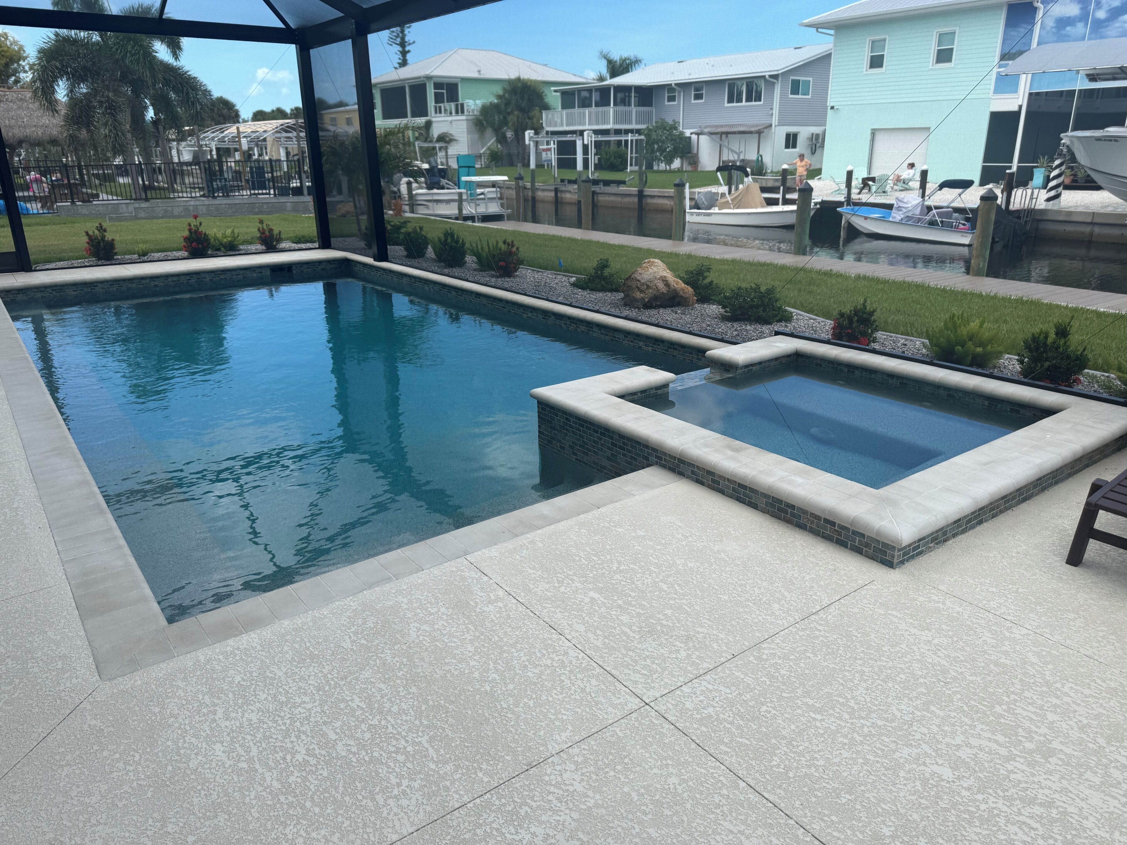 Piscina com uma pequena banheira de hidromassagem, rodeada por um terraço com vista para casas e um cais.